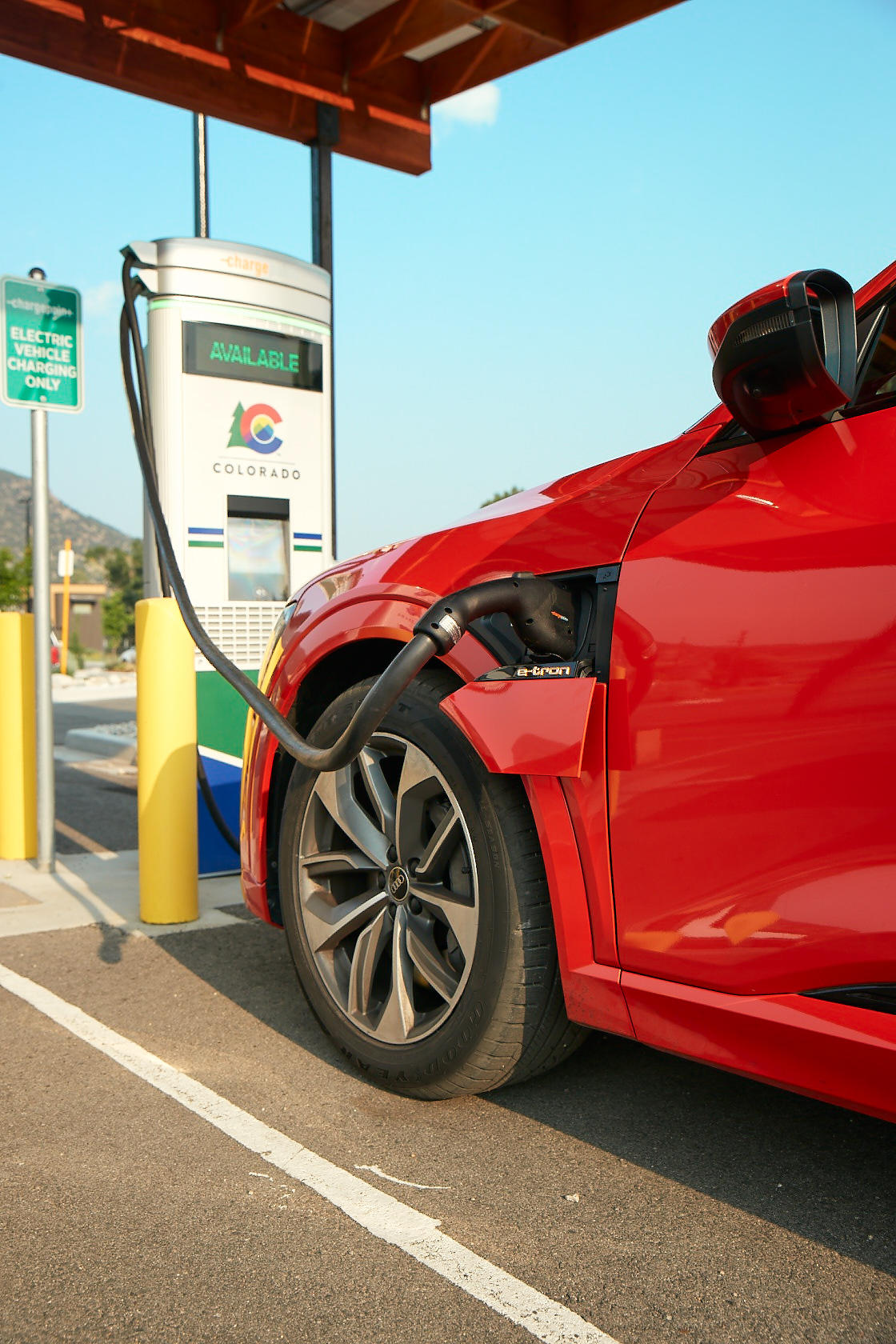 A red electric vehicle is plugged in getting ready to charge at a fast charging station with Colorado's state logo on it.