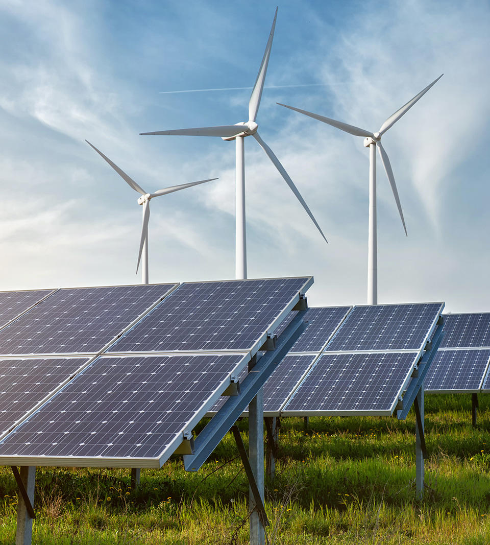 Solar Panels on a Grassy Field and Wind Turbines Against a Partly Cloudy Blue Sky