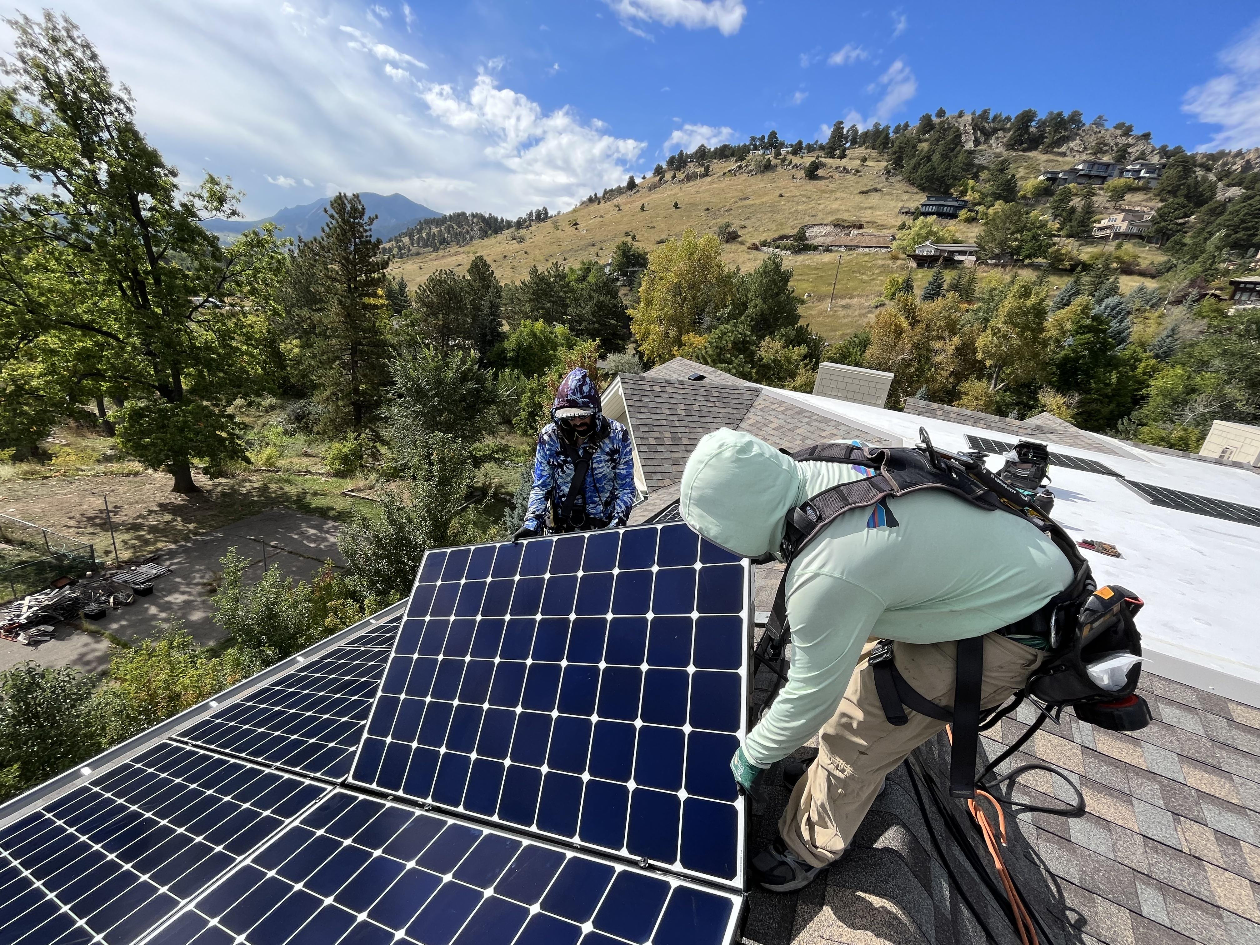 Two people install solar panels on a home's rooftop in Colorado's foothills.