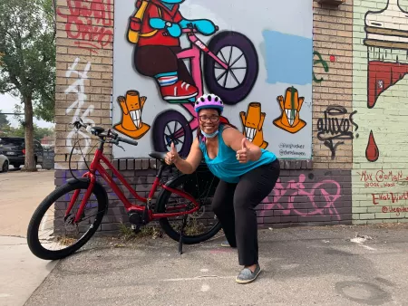 eBike program participant in front of her bike by urban bike shop mural
