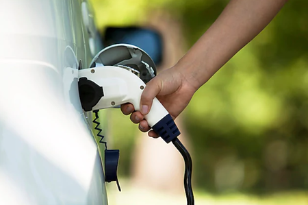 Hand of person shown charging a white electric vehicle