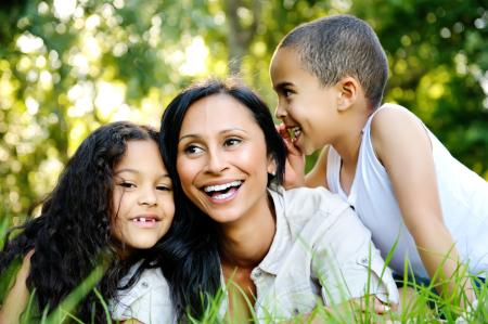 image of minority family - a mother with two children - a girl and a boy - laughing and shown on green grass
