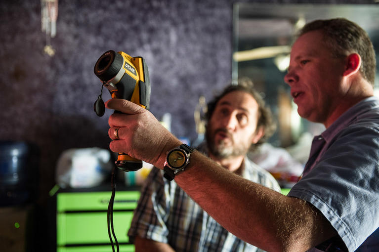 Two weatherization technicians use a thermal imaging camera to detect heat loss in a home.